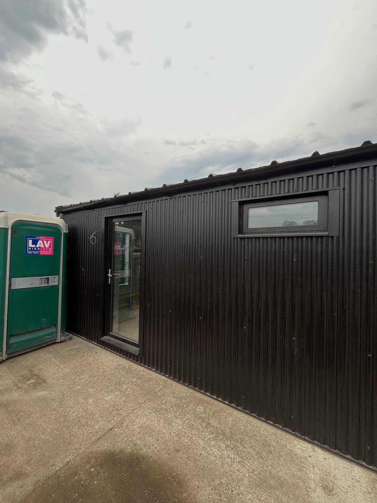 Finished garage conversion: black clad studio building with glazed door and windows