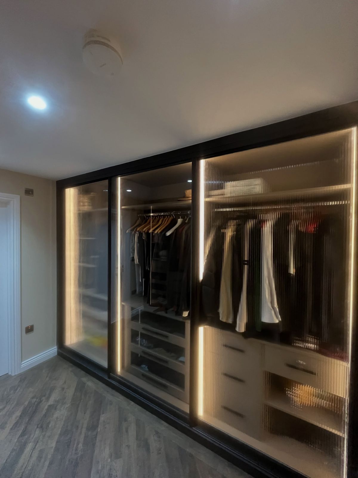 Lit walk-in wardrobe with glass doors